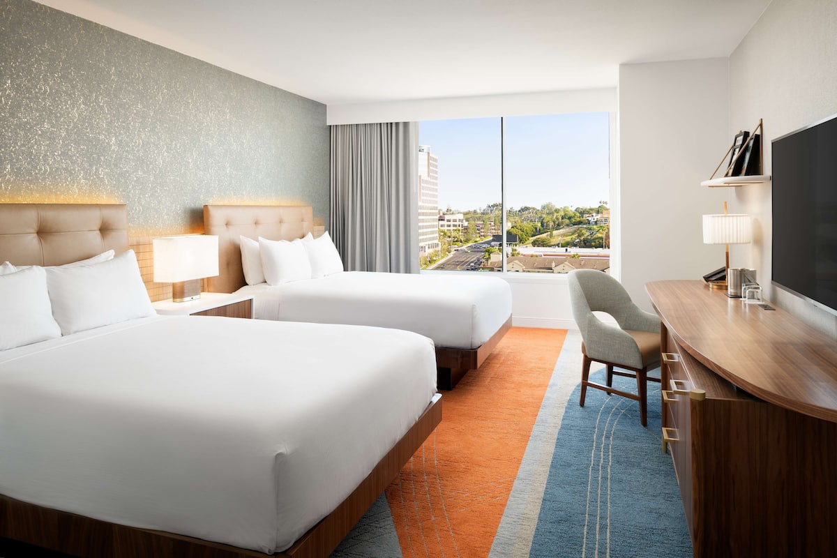Une chambre d’hôtel avec deux lits, un bureau, une télévision et une grande fenêtre donnant sur la ville.