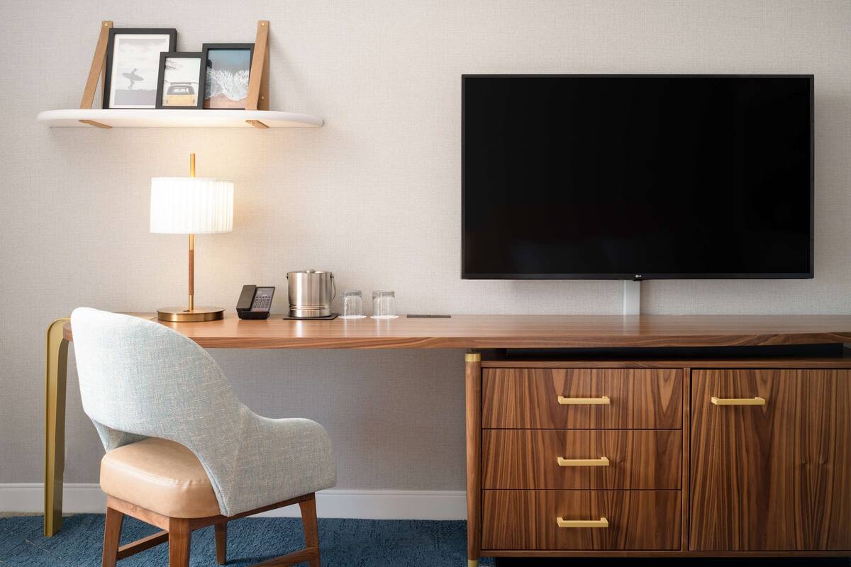 Une chambre d’hôtel équipée d’un bureau en bois, d’un téléviseur à écran plat, d’une chaise, d’une lampe et d’une machine à café.