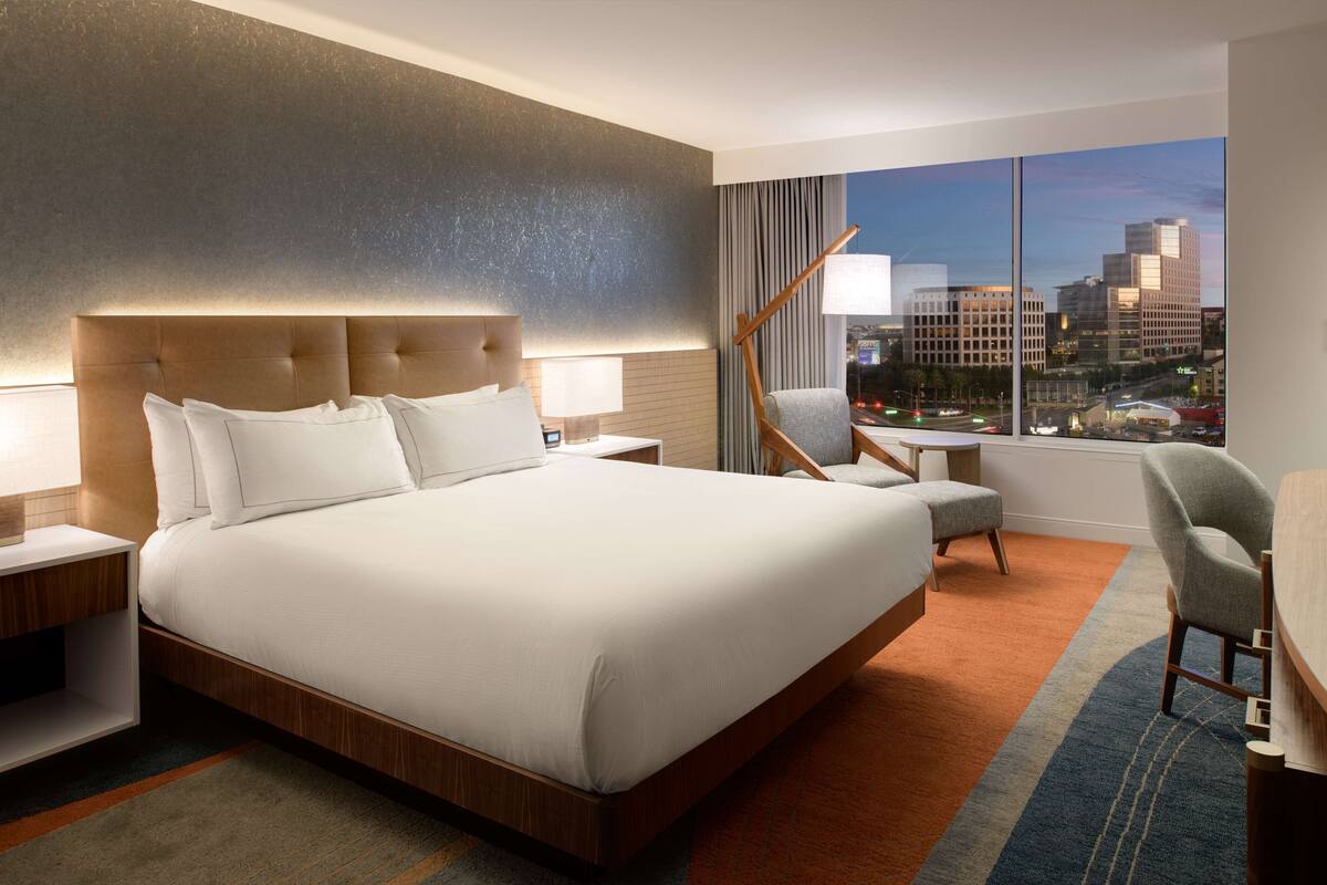 Une chambre d’hôtel moderne, dotée d’un grand lit, d’un bureau et offrant une vue sur le paysage urbain.