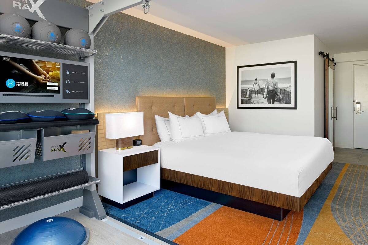 Une chambre d’hôtel équipée d’un lit, d’un bureau avec un ordinateur, d’un tapis de course et d’un téléviseur fixé au mur.