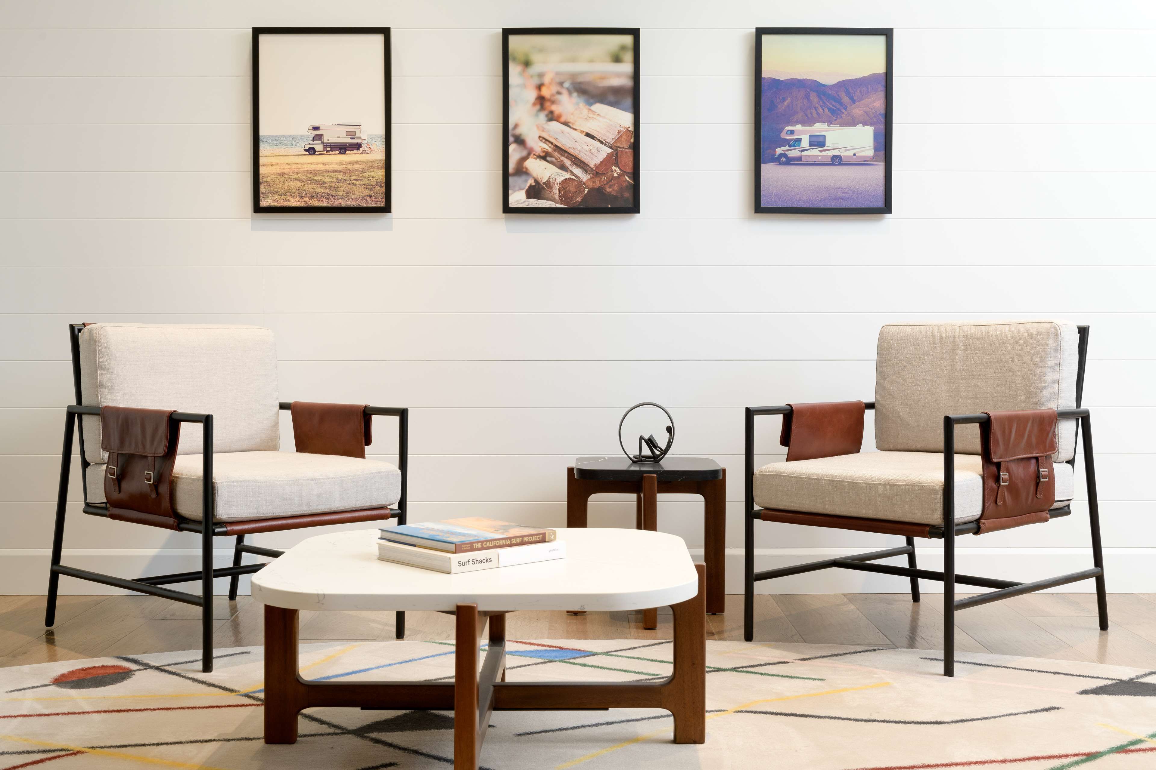 Una habitación con dos sillones de cuero, una mesita pequeña y tres cuadros en la pared.