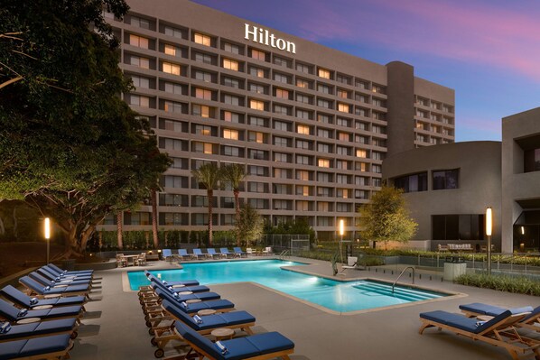 Un hôtel doté d’une piscine, de chaises longues et d’un grand bâtiment sur lequel on peut lire l’inscription « Hilton ».