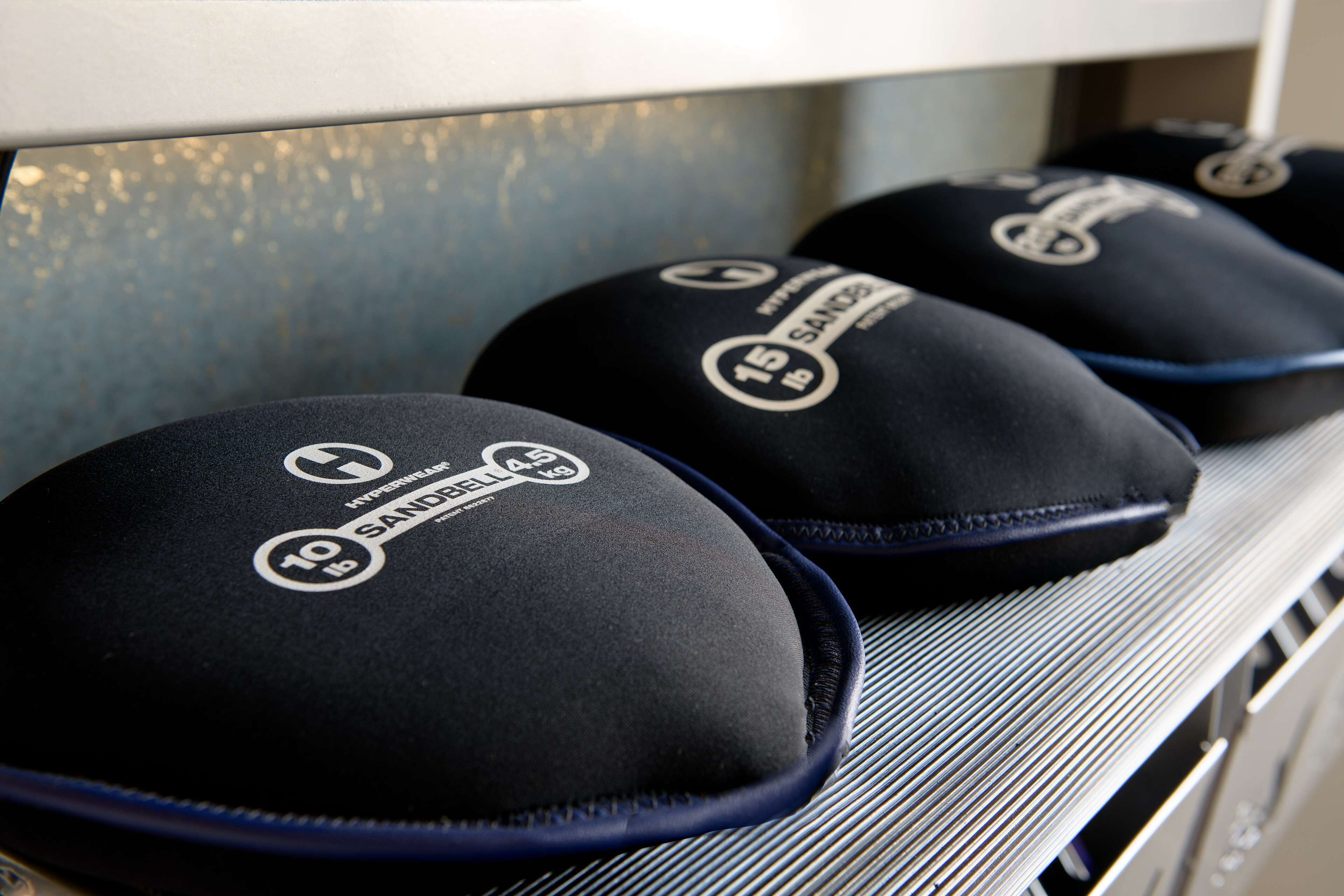 A shelf with three black caps labeled "Hyperwear" and "SANDBELT" with weight markings.