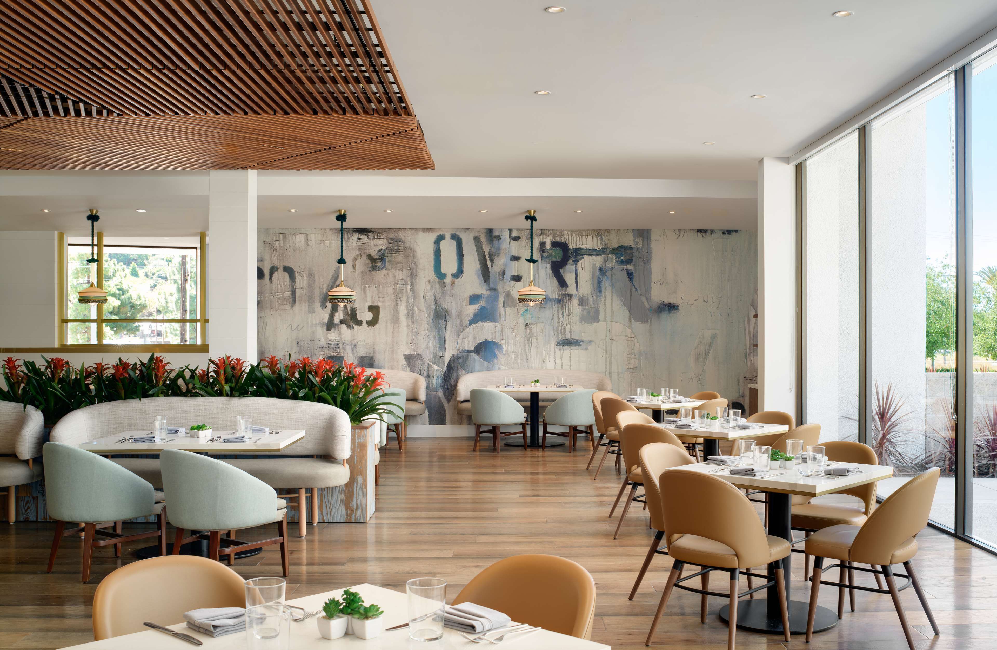 A modern restaurant with a wooden ceiling, large windows, and a mural on the back wall.