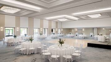 Un amplio salón de banquetes, bien iluminado, con varias mesas redondas dispuestas para eventos, cubiertas con manteles blancos y sillas transparentes.