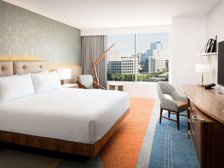 Een hotelkamer met een groot bed, een bureau met een televisie en uitzicht op de stad.