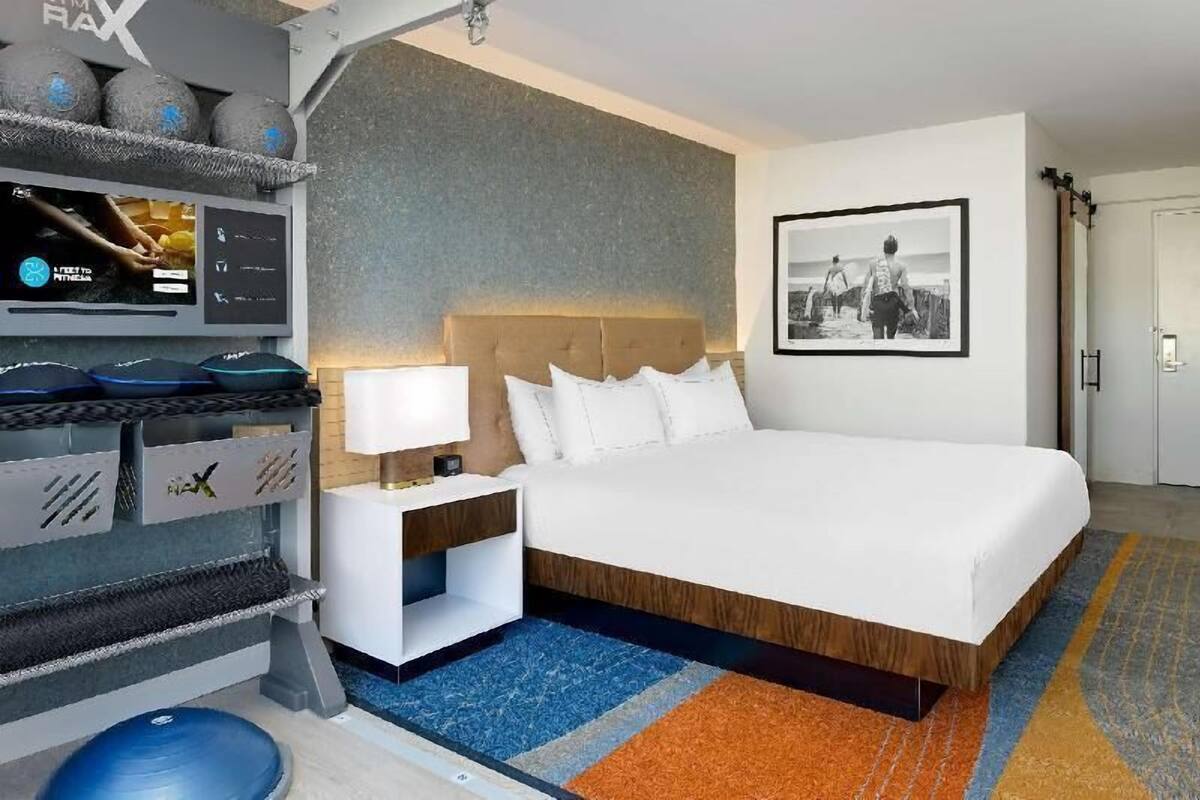 Une chambre d’hôtel moderne avec un grand lit, une table de chevet avec une lampe, un téléviseur fixé au mur et un tableau encadré.