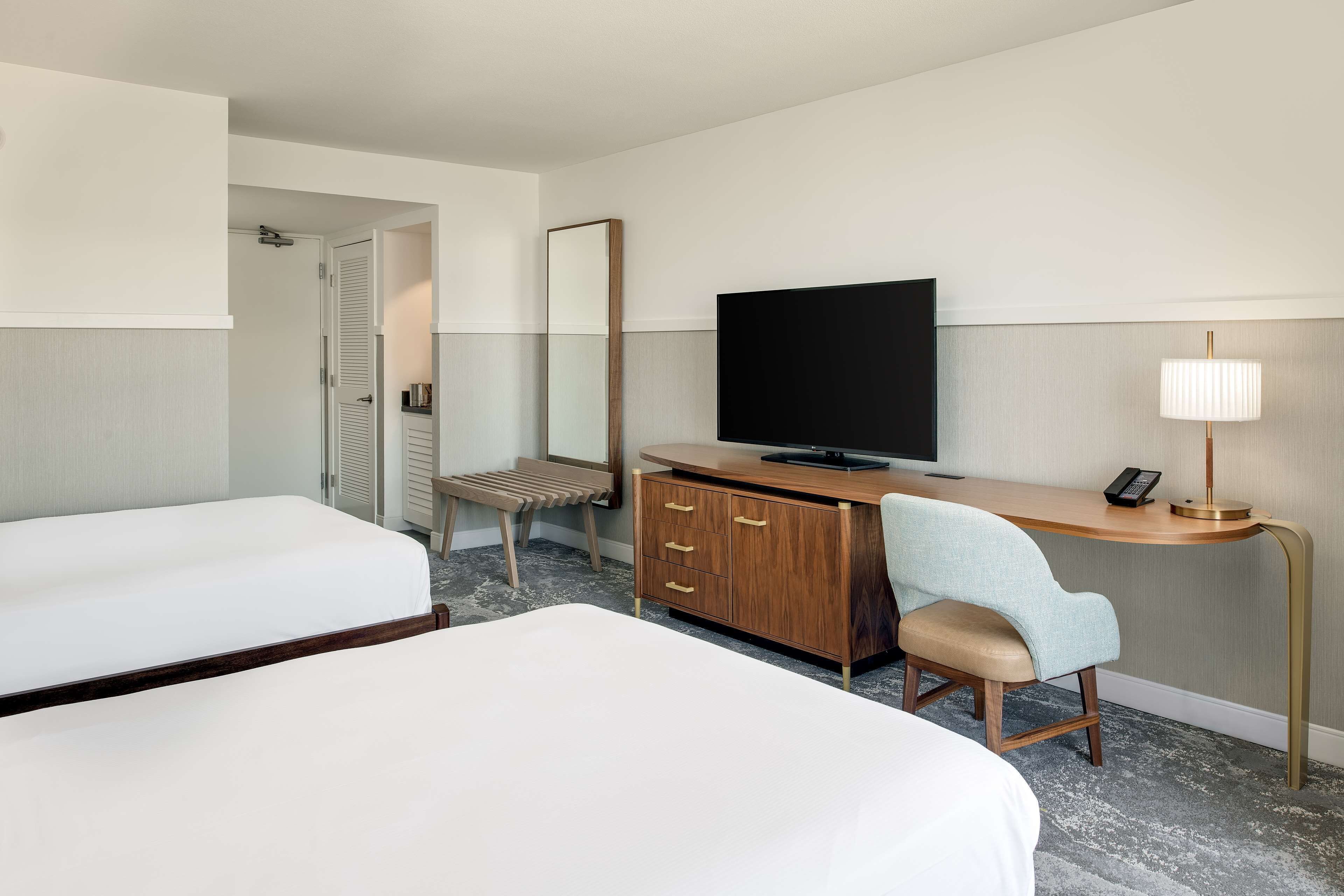 Een hotelkamer met twee bedden, een bureau met een televisie, een spiegel en een lamp.
