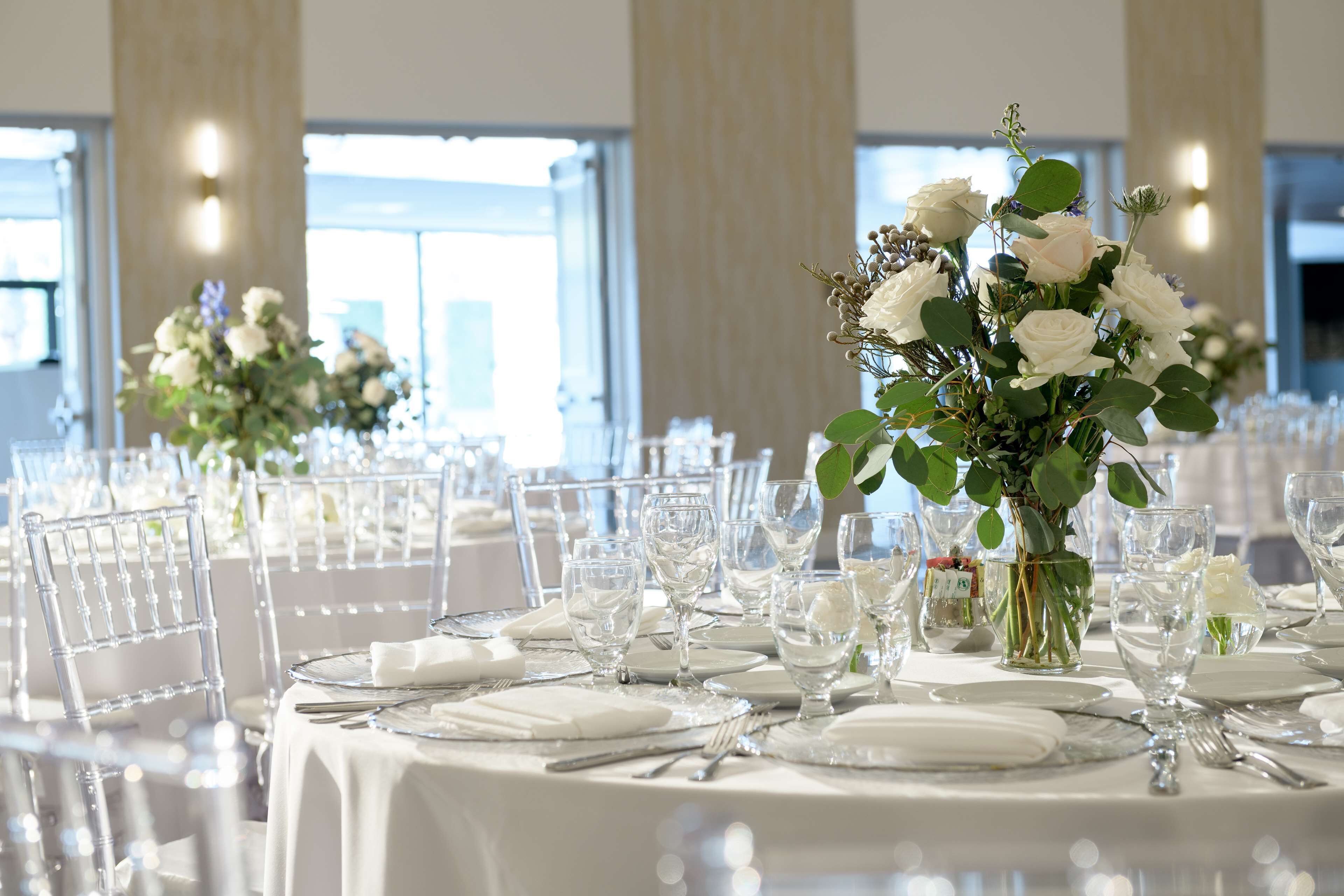 A banquet hall with round tables set for a formal event, featuring white tablecloths, glassware, and floral centerpieces.