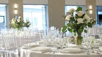 A banquet hall with round tables set for a formal event, featuring white tablecloths, glassware, and floral centerpieces.