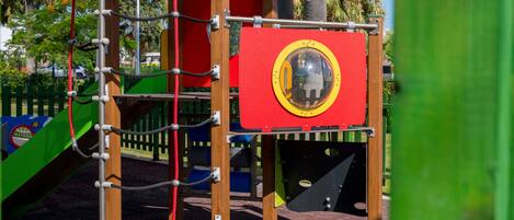 A playground structure with a climbing area, a slide, and a red platform with a yellow circle.