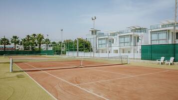 A tennis court with a net, surrounded by a fence, and adjacent to a building with multiple floors and balconies.