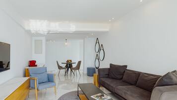 Ein modernes Wohnzimmer mit Sofa, Couchtisch, Fernseher und einem Essbereich mit Stühlen und Tisch.