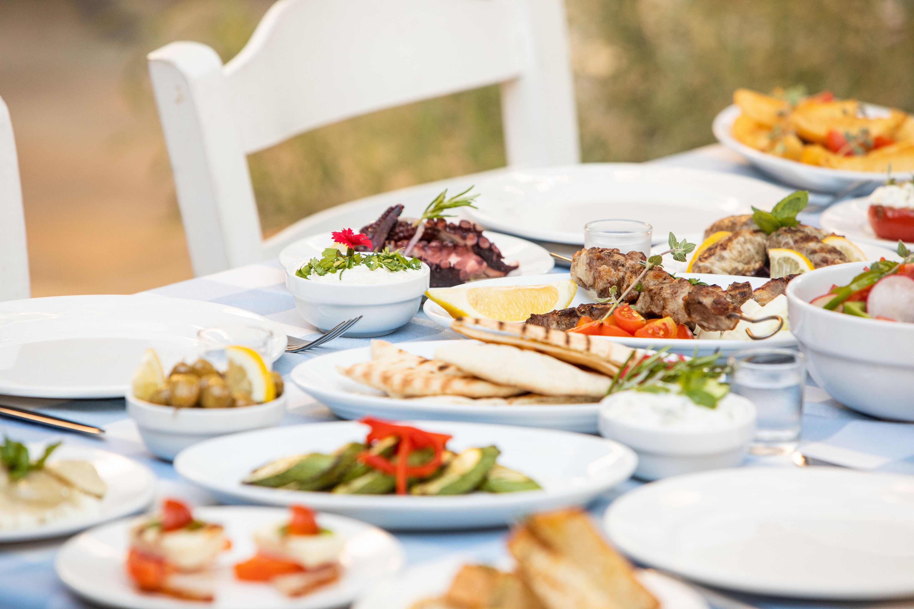 Una mesa dispuesta con varios platos, incluyendo carne a la parrilla, ensaladas y pan plano, indicando una preparación para comer.
