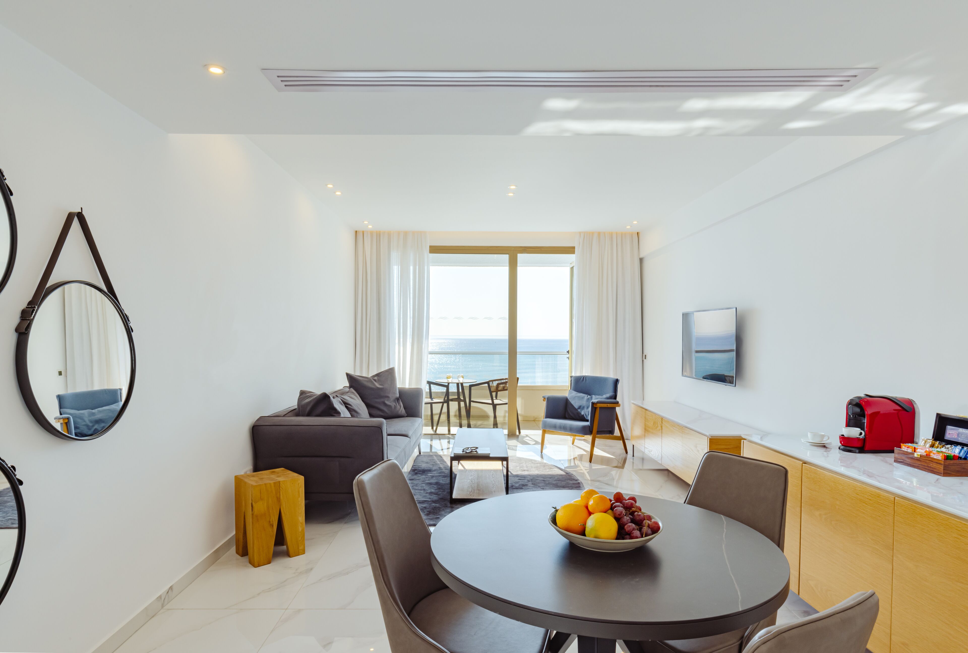 A modern living room with a dining area, a sofa, a coffee table, and a view of the sea.