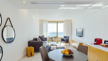A modern living room with a dining area, a sofa, a coffee table, and a view of the sea.