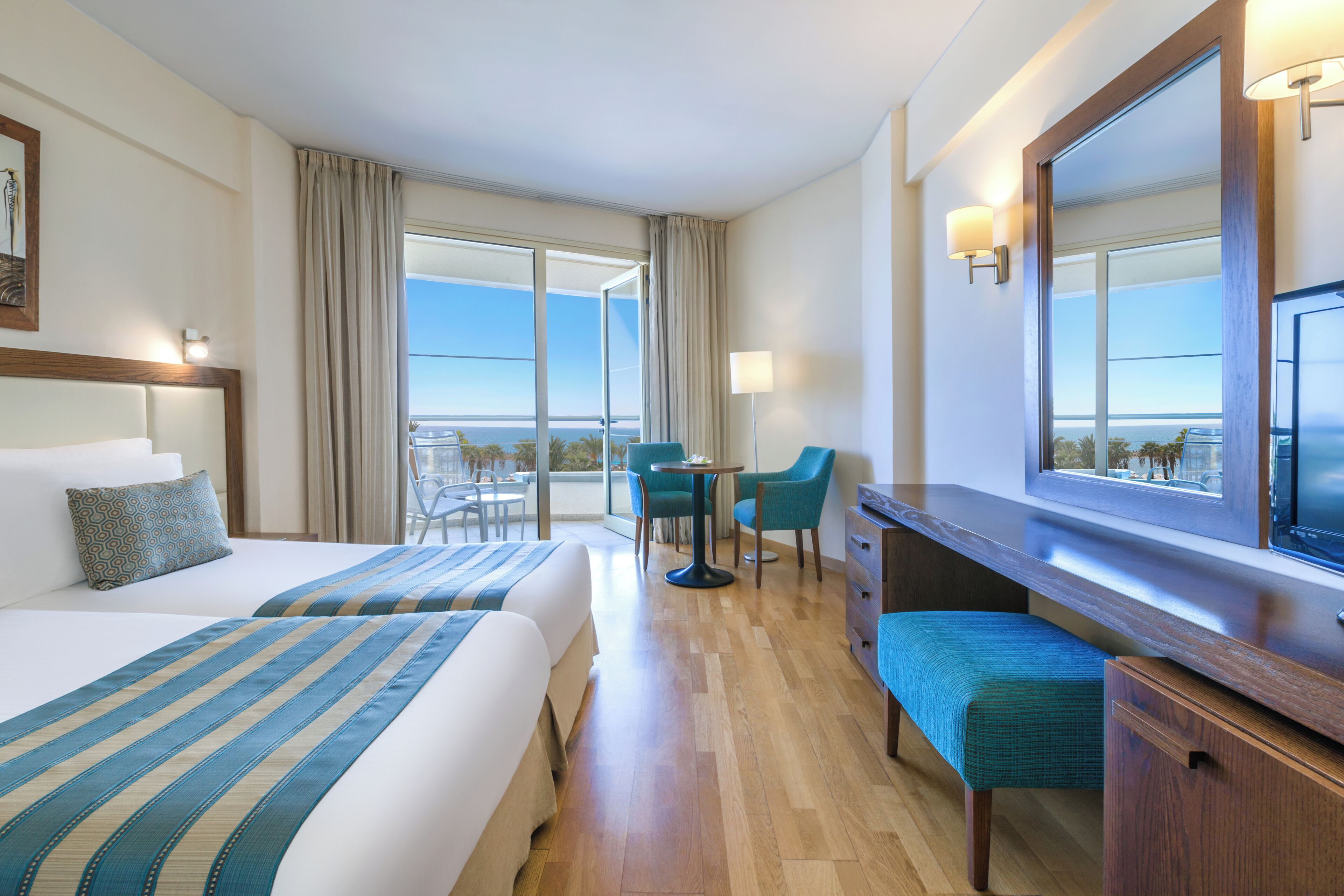 Habitación de hotel con dos camas, un escritorio, una silla, una mesita y un ventanal con vistas.