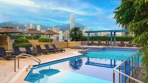 A rooftop pool with lounge chairs and umbrellas, surrounded by cityscape views.