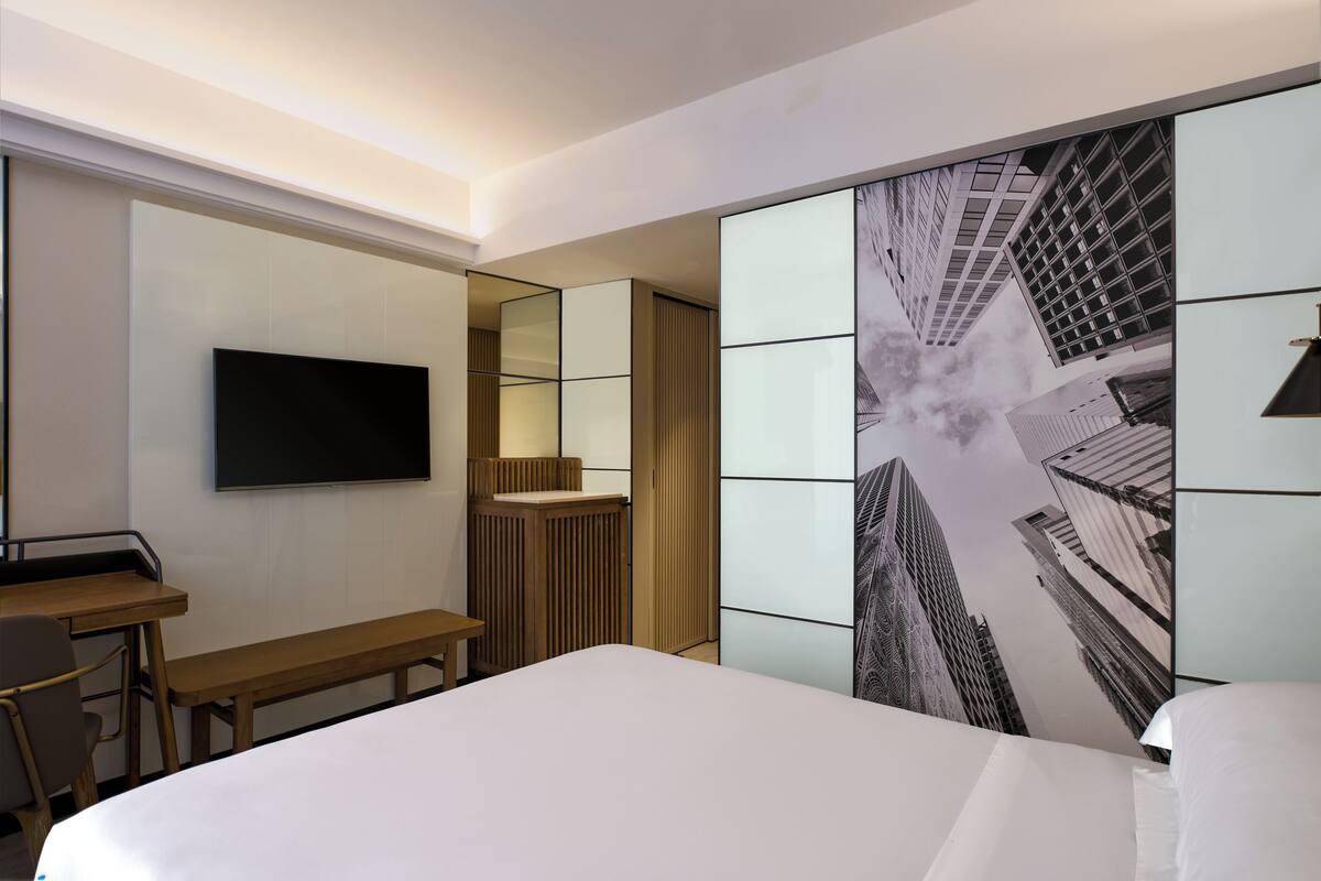 A hotel room with a bed, a desk, a chair, a TV, and a large mirror.