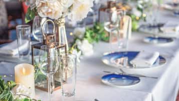 A table set with blue plates, silverware, and clear glassware, adorned with white flowers and candles.