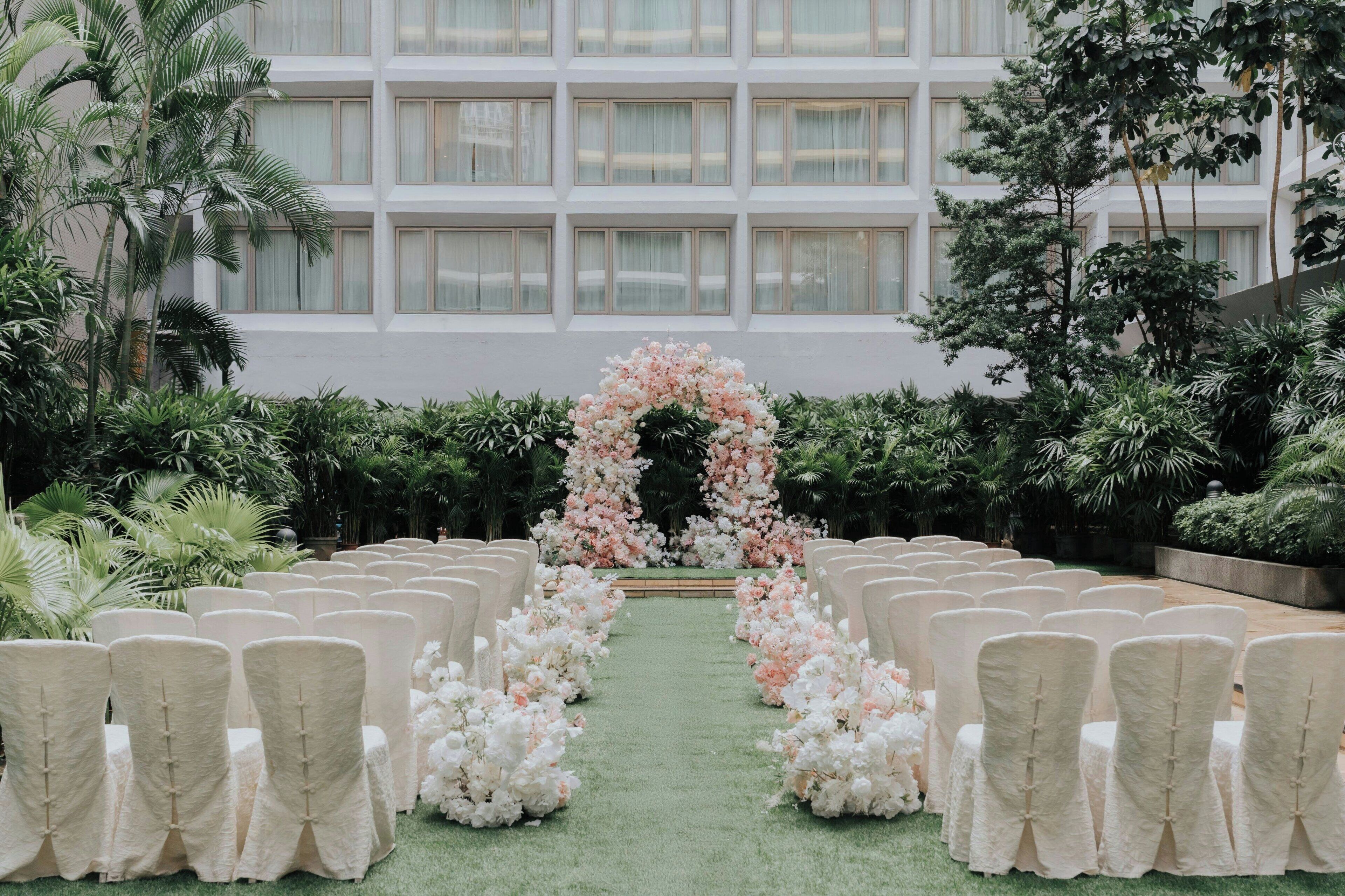 An outdoor wedding aisle with white chairs and a floral arch.