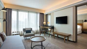 A modern hotel room with a sofa, a round table, a desk, a TV, and a bed.