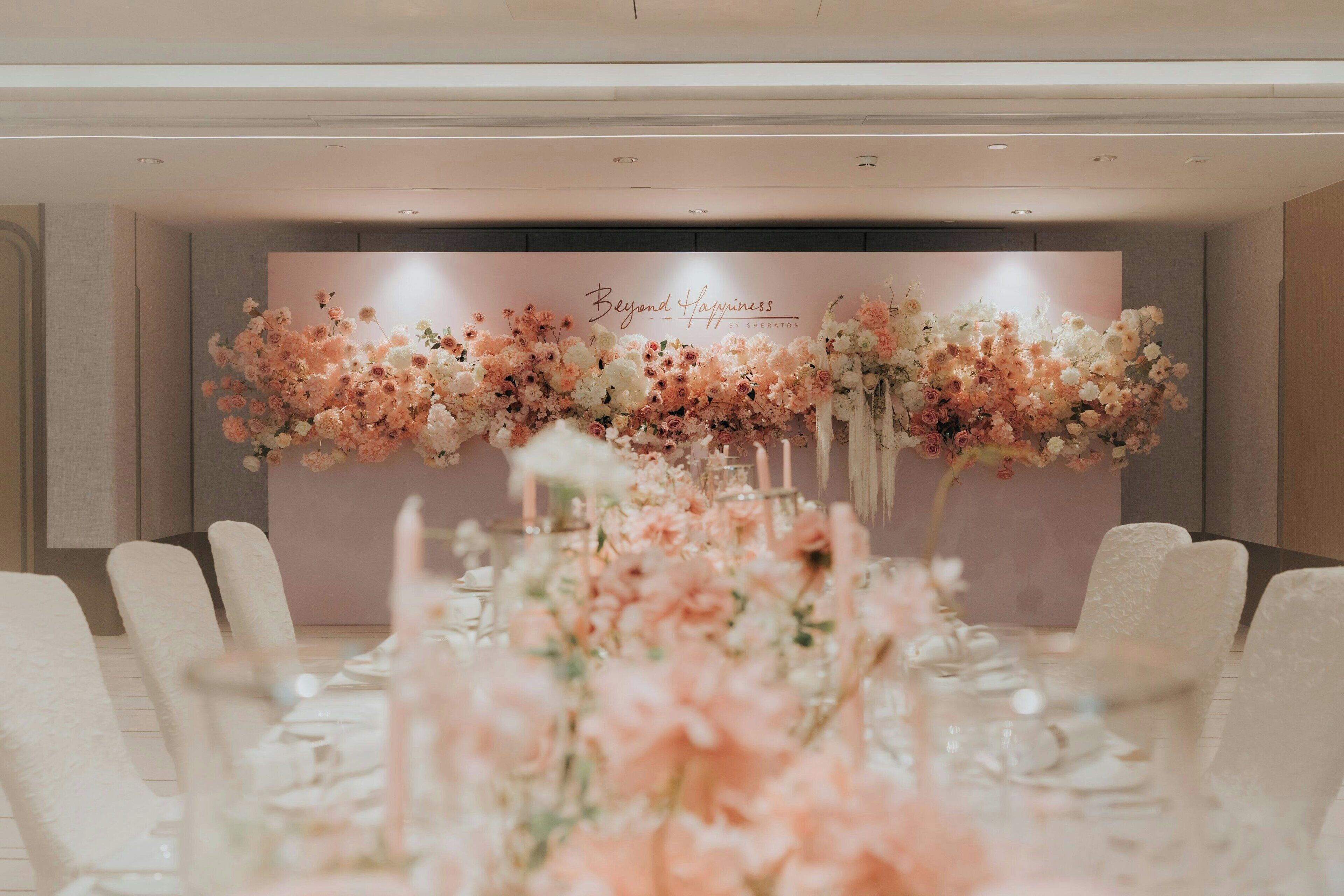 Ett långt bord med vita stolar, dekorerat med blomsterarrangemang och ljus.