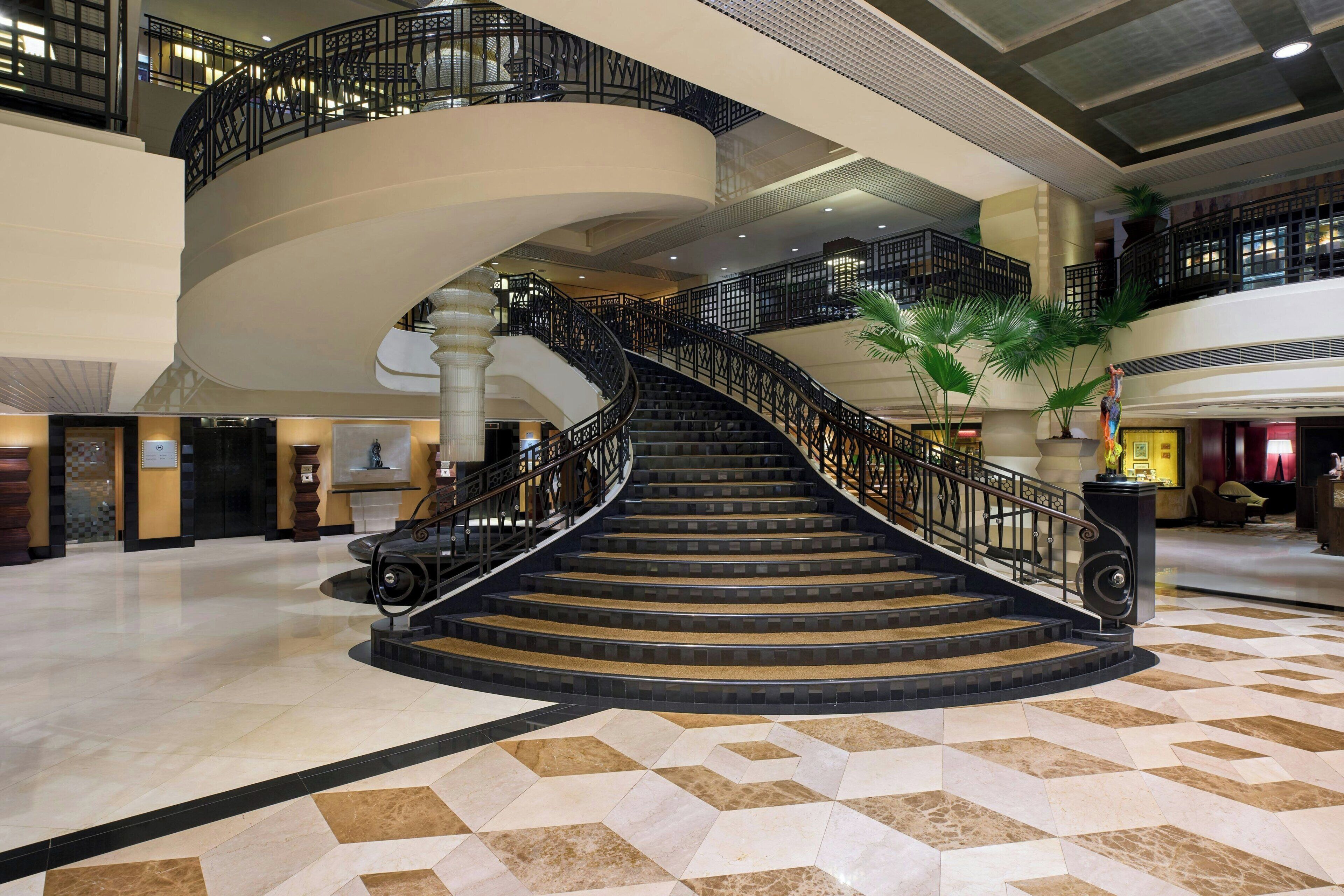 A grand spiral staircase in a hotel lobby with a geometric tile floor and black railings.