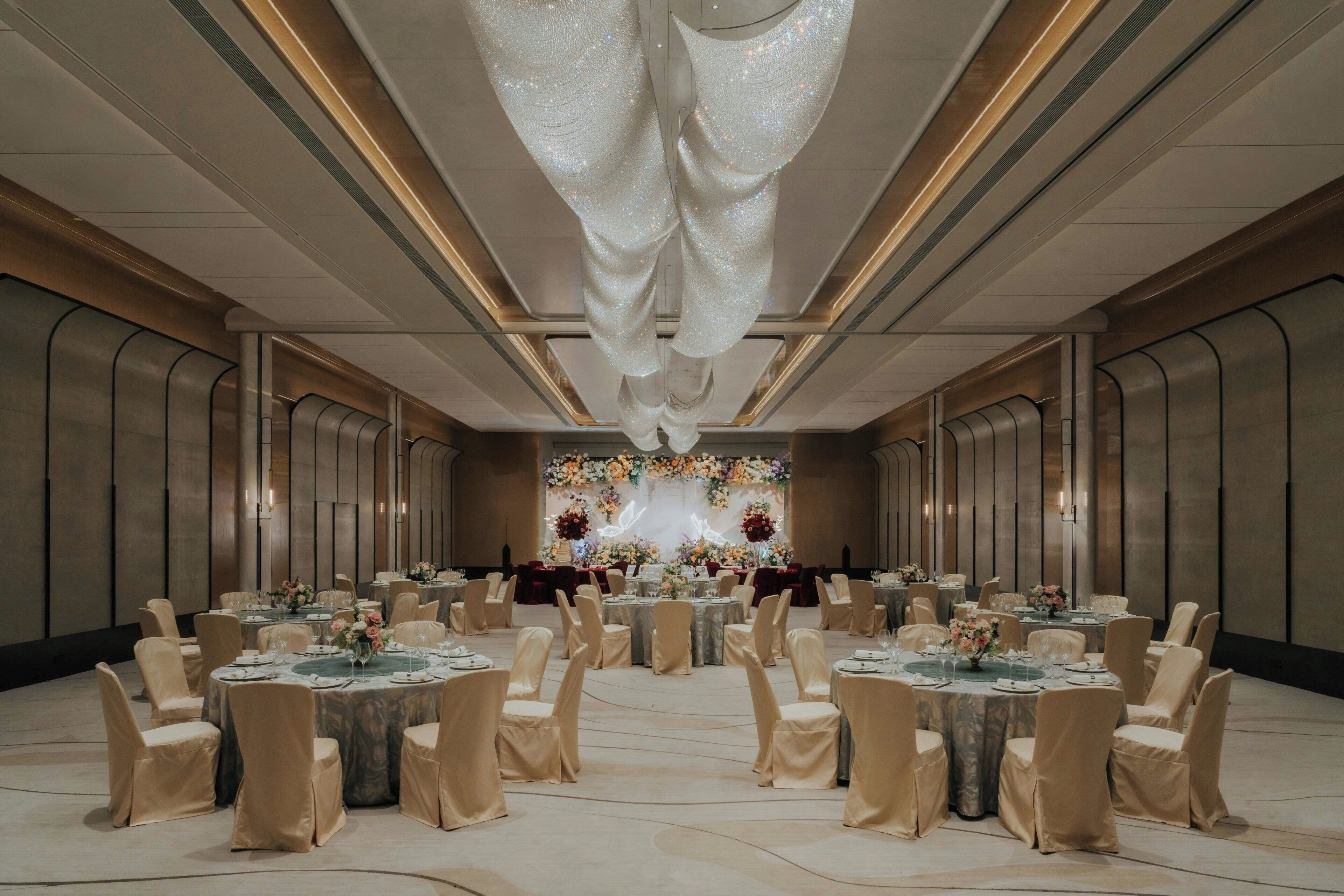 A banquet hall with round tables, chairs, and a floral backdrop.