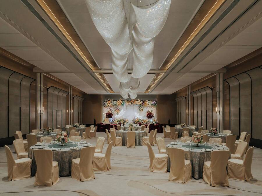 A banquet hall with round tables, chairs, and a floral backdrop.