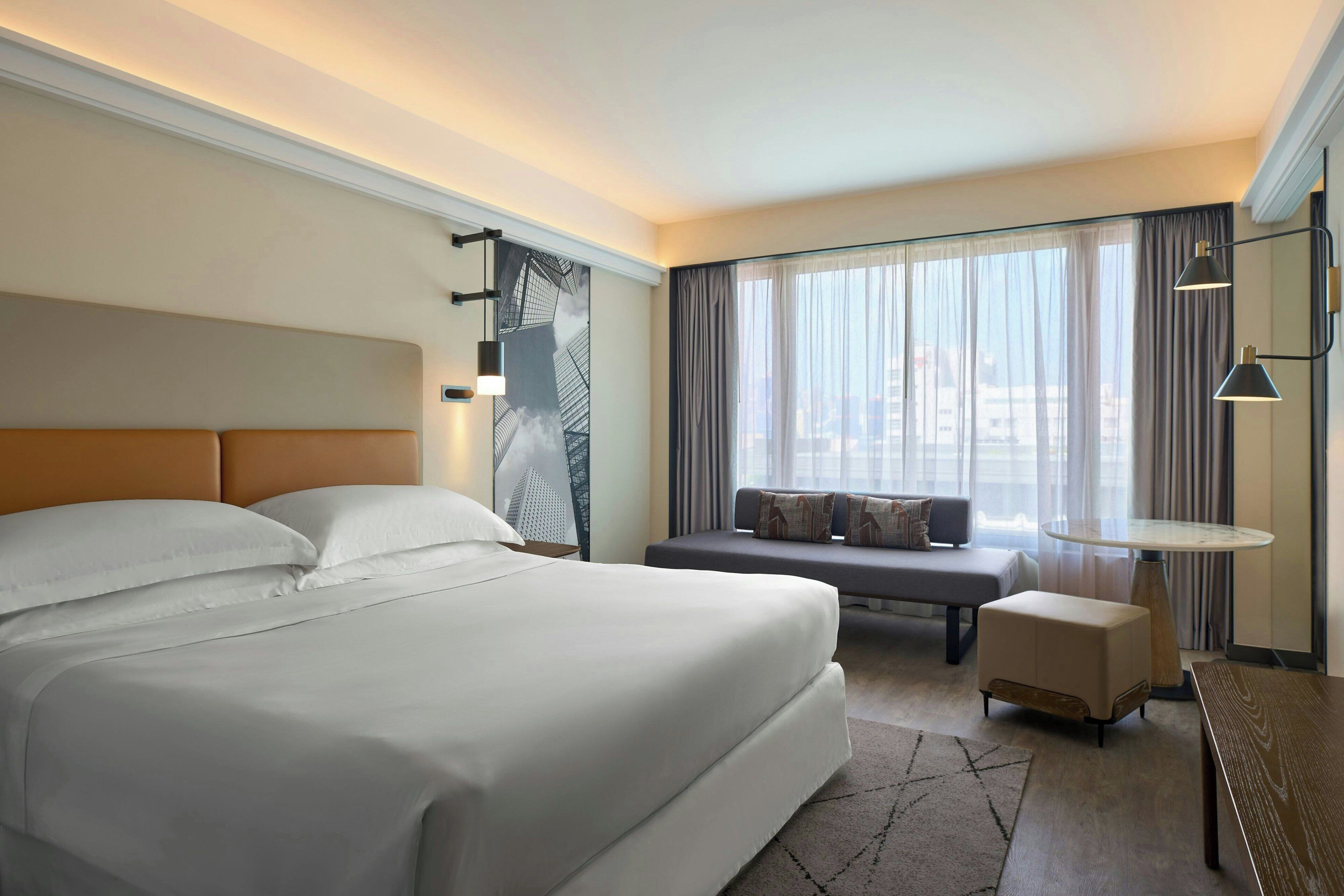 Een hotelkamer met een groot bed, een bank, een tafeltje en uitzicht op de stad door grote ramen.