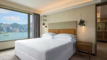 A hotel room with a large bed, a nightstand, a lamp, and a view of a cityscape and water.