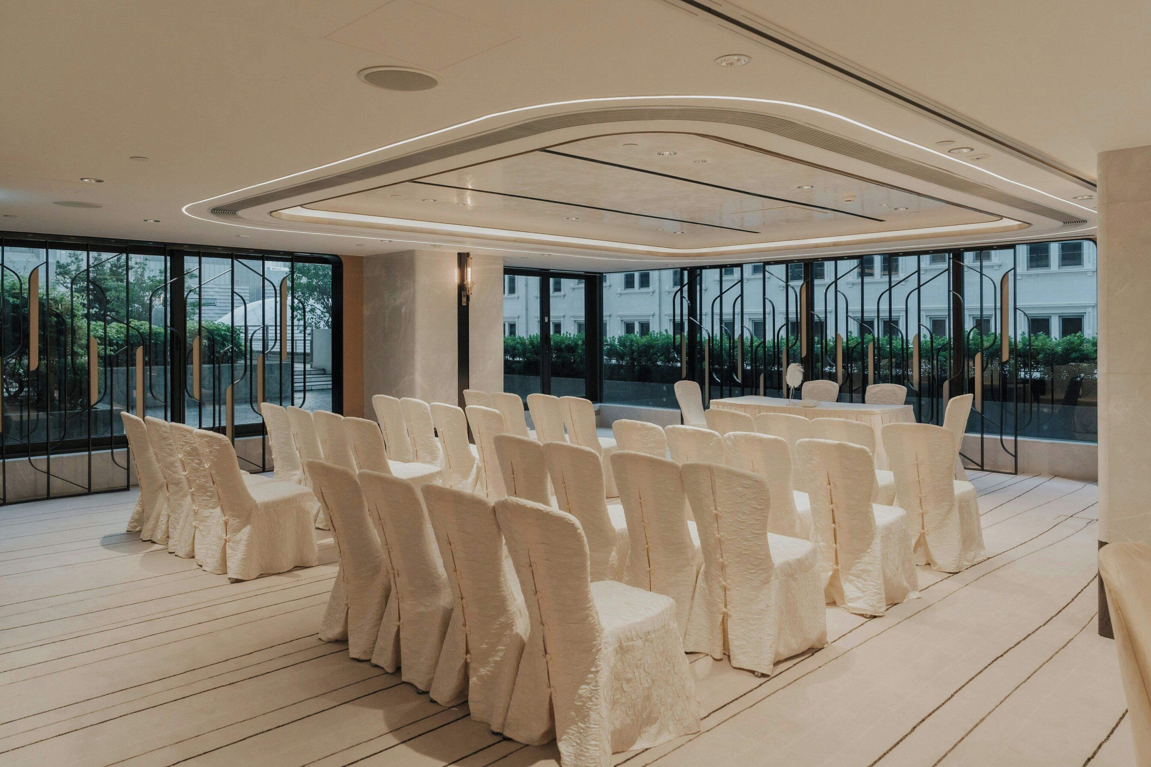 A conference room with rows of white chairs, large windows, and a modern ceiling design.