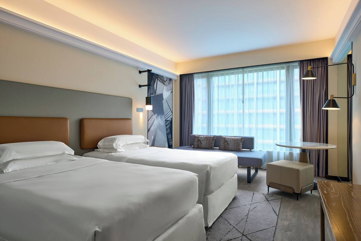 A hotel room with two beds, a sofa, a small table, and a large window with curtains.
