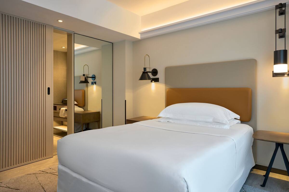 A modern hotel room with a large bed, a walk-in closet, and a bathroom with a mirror and towel rack.