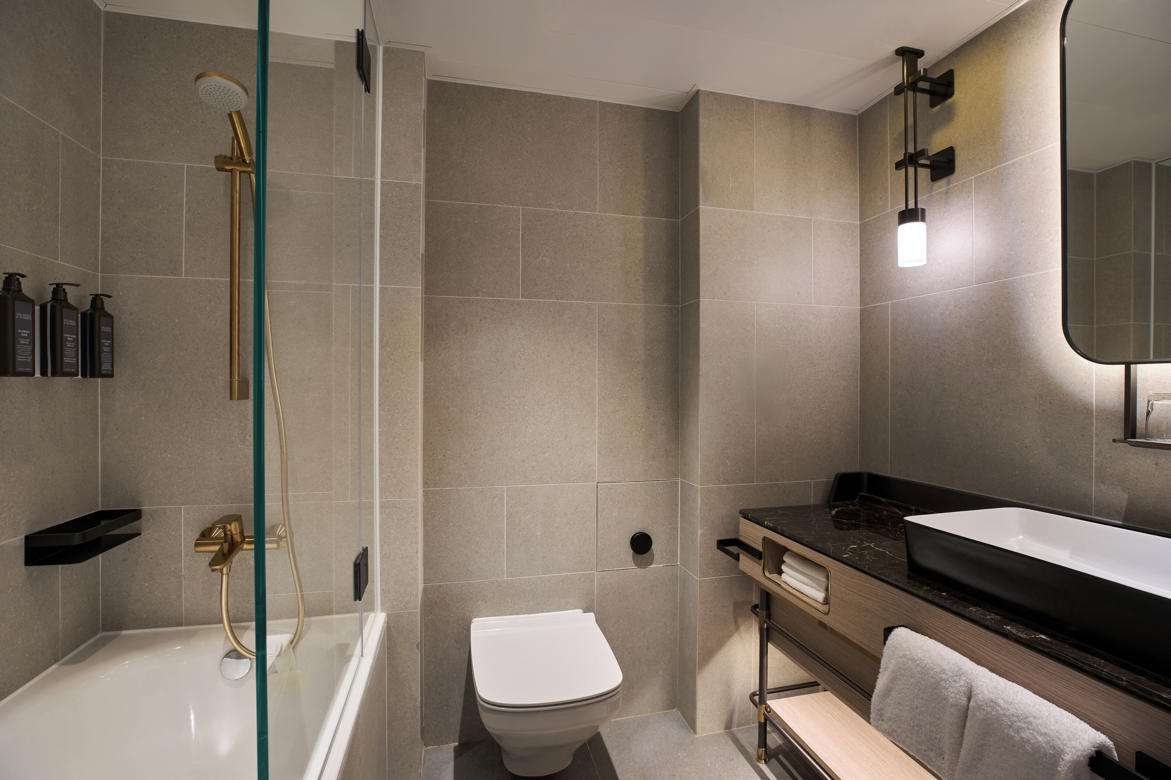 A modern bathroom with a glass-enclosed shower, a white toilet, a black sink, and a mirror.
