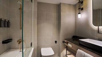 A modern bathroom with a glass-enclosed shower, a white toilet, a black sink, and a mirror.