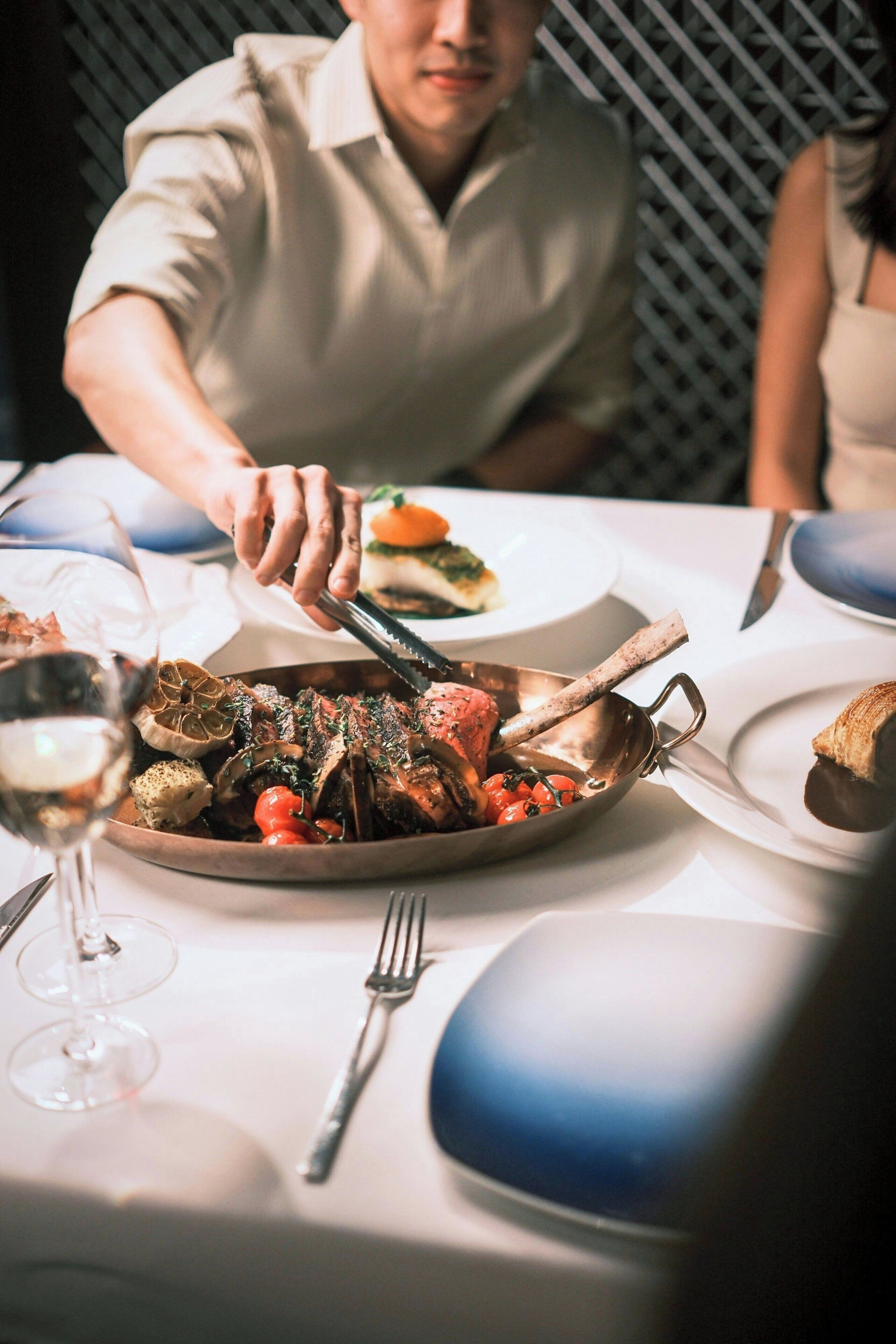 A dining table with a roasted duck, wine glasses, and cutlery.