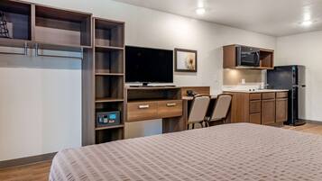 Habitación de hotel pequeña con cama, escritorio, silla, televisión, microondas y refrigerador.
