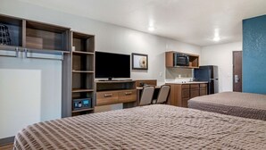 A hotel room with two beds, a TV, a desk with a chair, a microwave, a refrigerator, and a wardrobe.