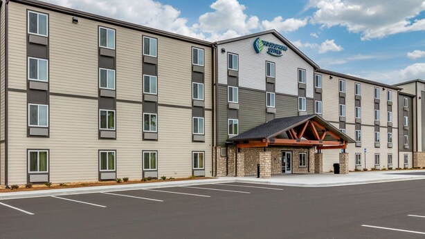 A multi-story hotel with a flat roof and a sign reading "Woodspring Suites".