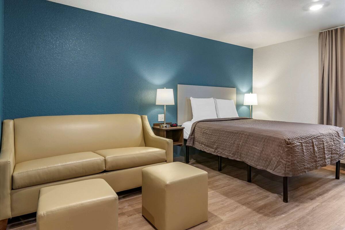 A hotel room with a bed, a sofa, a nightstand, and a lamp.