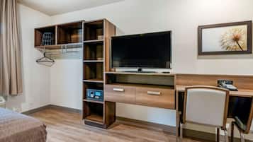 A hotel room with a bed, a desk with a chair, a TV, and a bookshelf.