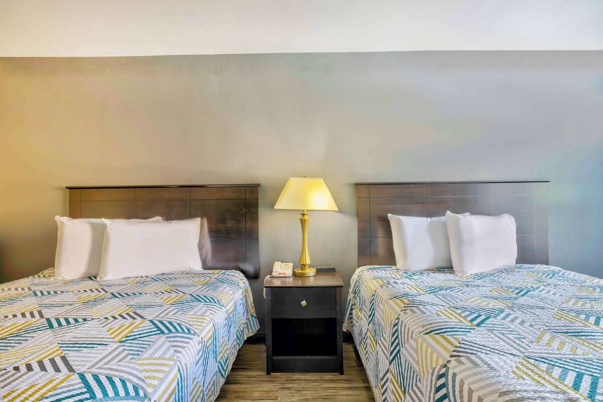 A hotel room with two beds, each with a patterned bedspread, a bedside table with a lamp, and a nightstand with a phone.