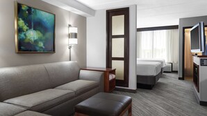 Habitación de hotel con sofá, una mesita, televisión, cama y un cuadro en la pared.