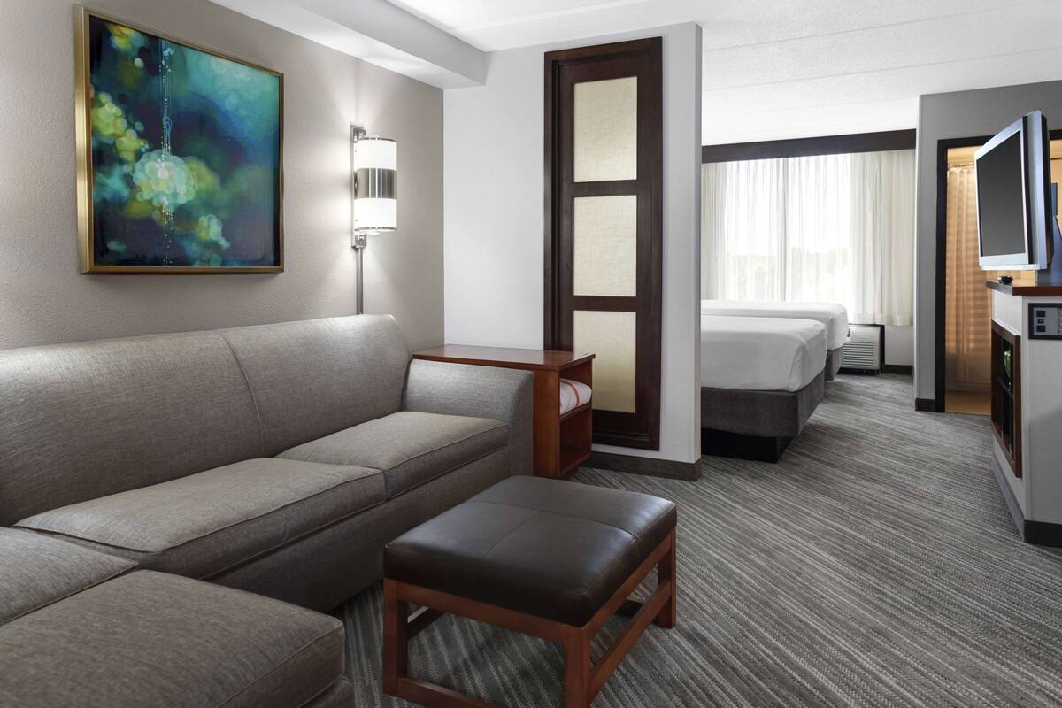 Een hotelkamer met een bank, een eettafeltje, een televisie, een bed en een schilderij aan de muur.