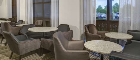 Un vestíbulo de hotel con varias zonas de estar, incluyendo sofás y mesas redondas, y amplias ventanas con cortinas.