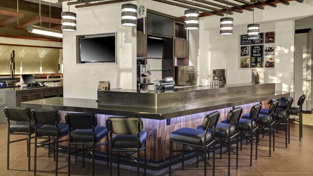 Una zona de bar moderna con una barra central, taburetes y un panel de menú.
