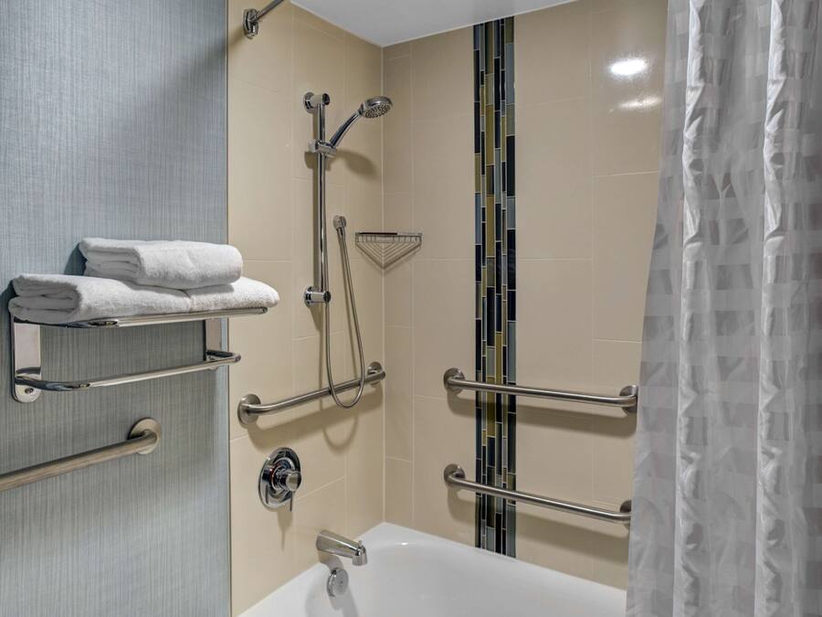 A modern bathroom with a bathtub, grab bars, a showerhead, and a towel rack.