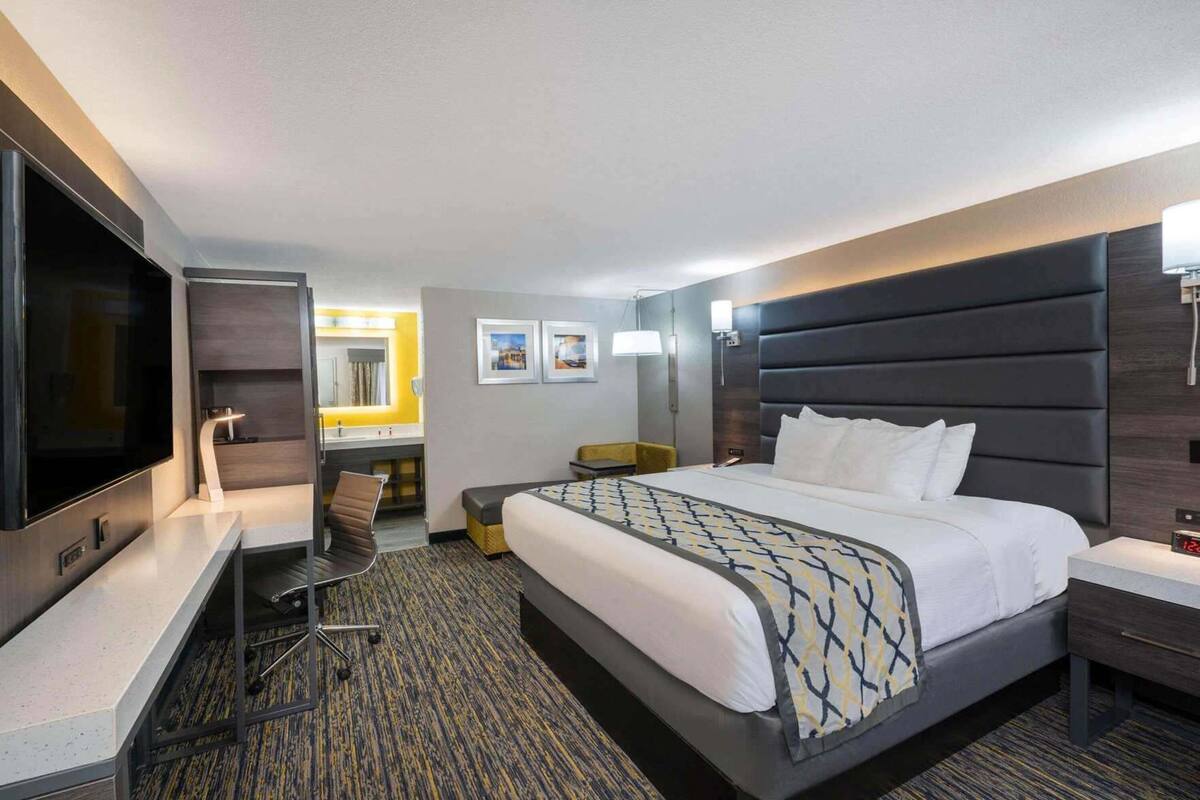 Habitación de hotel con cama, escritorio, silla, televisión, baño y mesita de noche.